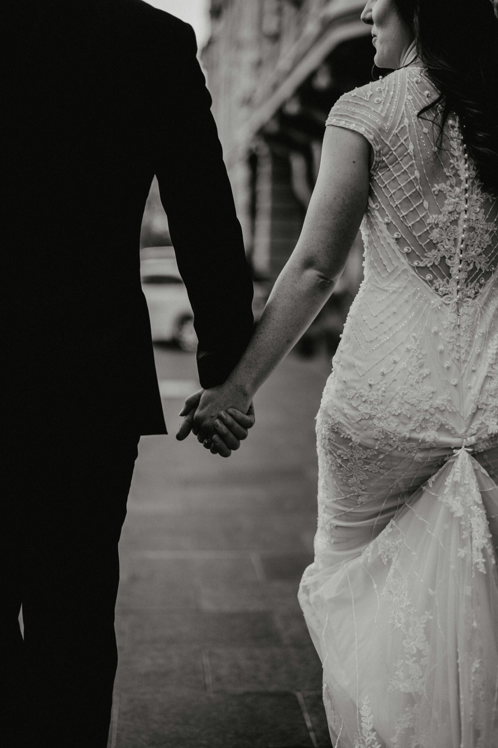 Close-up of bride and groom holding hands, bride in beaded lace gown at Cotswolds wedding