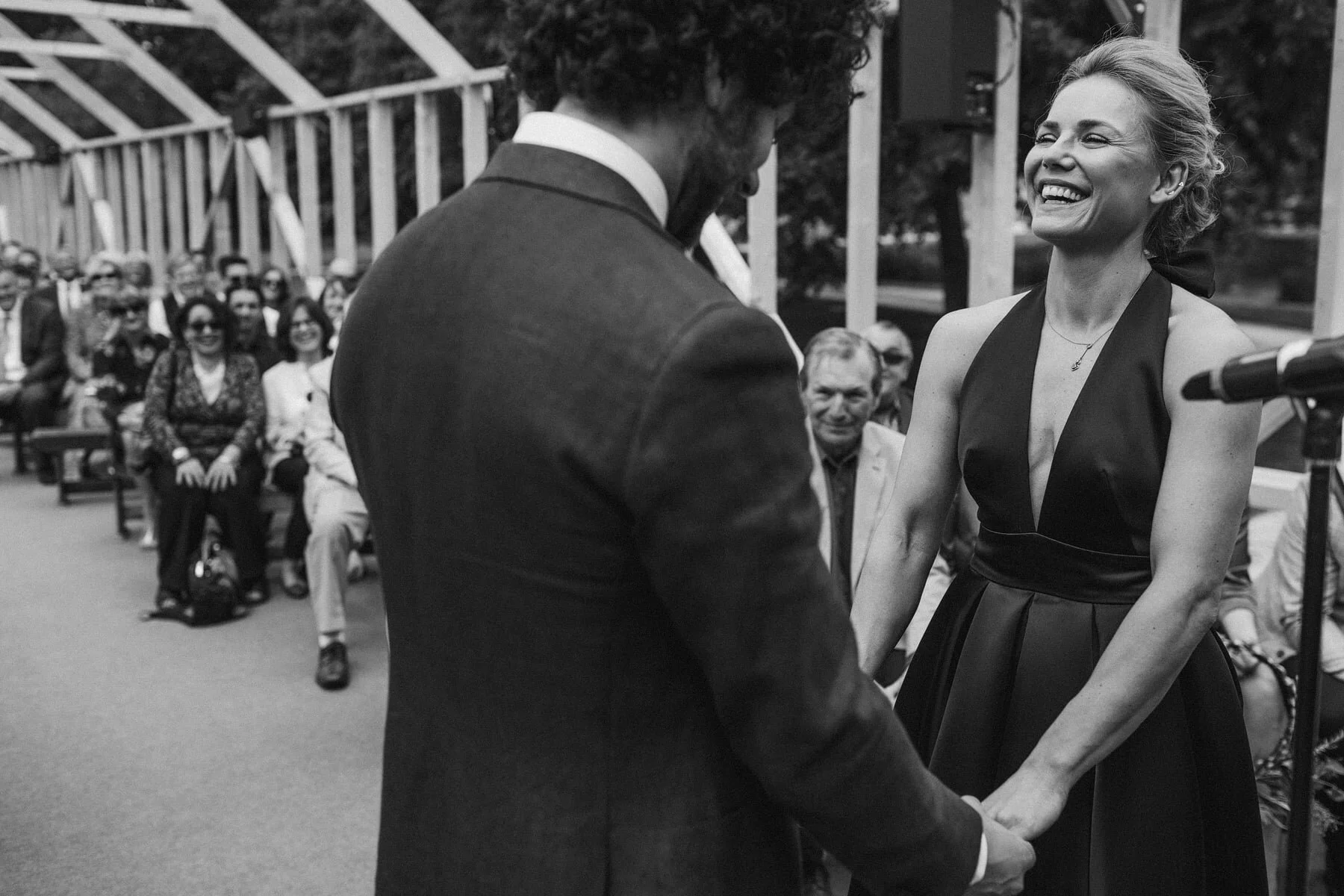 Groom walking with smiling guest at outdoor Cotswolds wedding, candid black and white photo